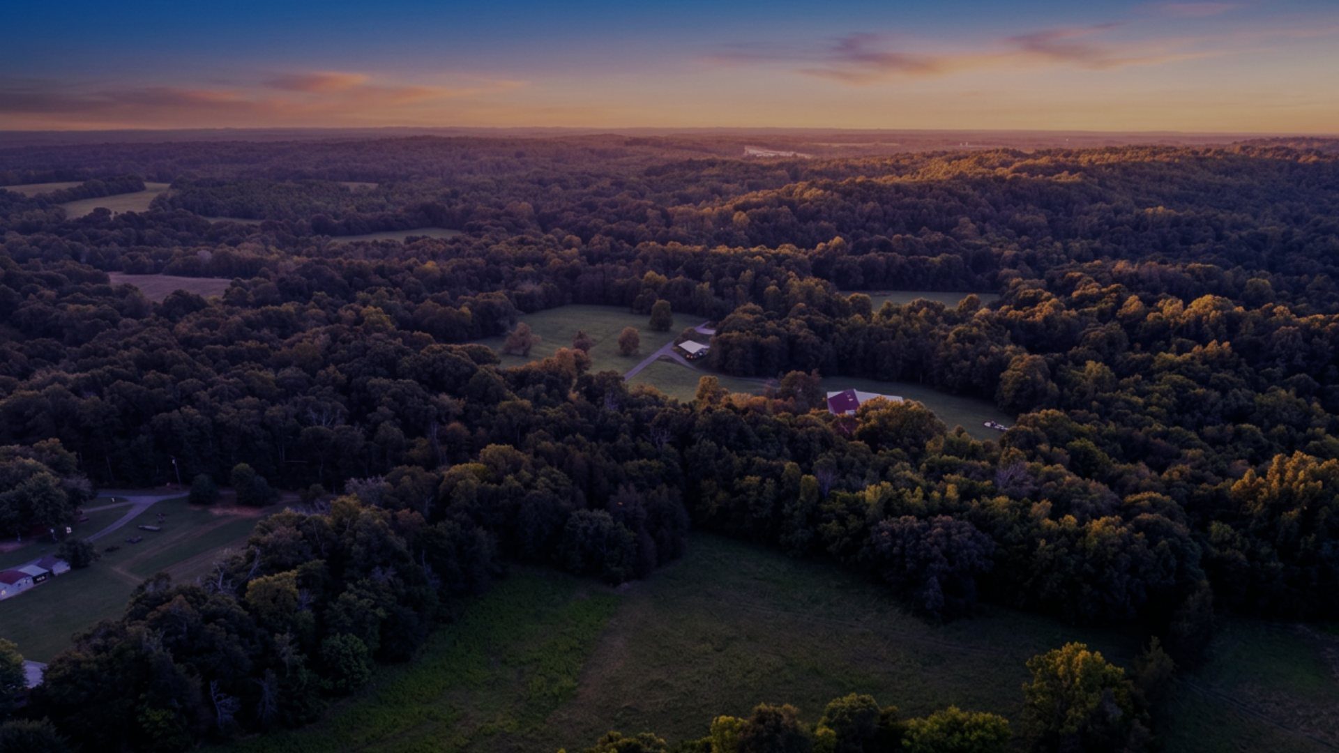 Golden-hour aerial over rolling forest, pasture and homesteads — Biggers Road