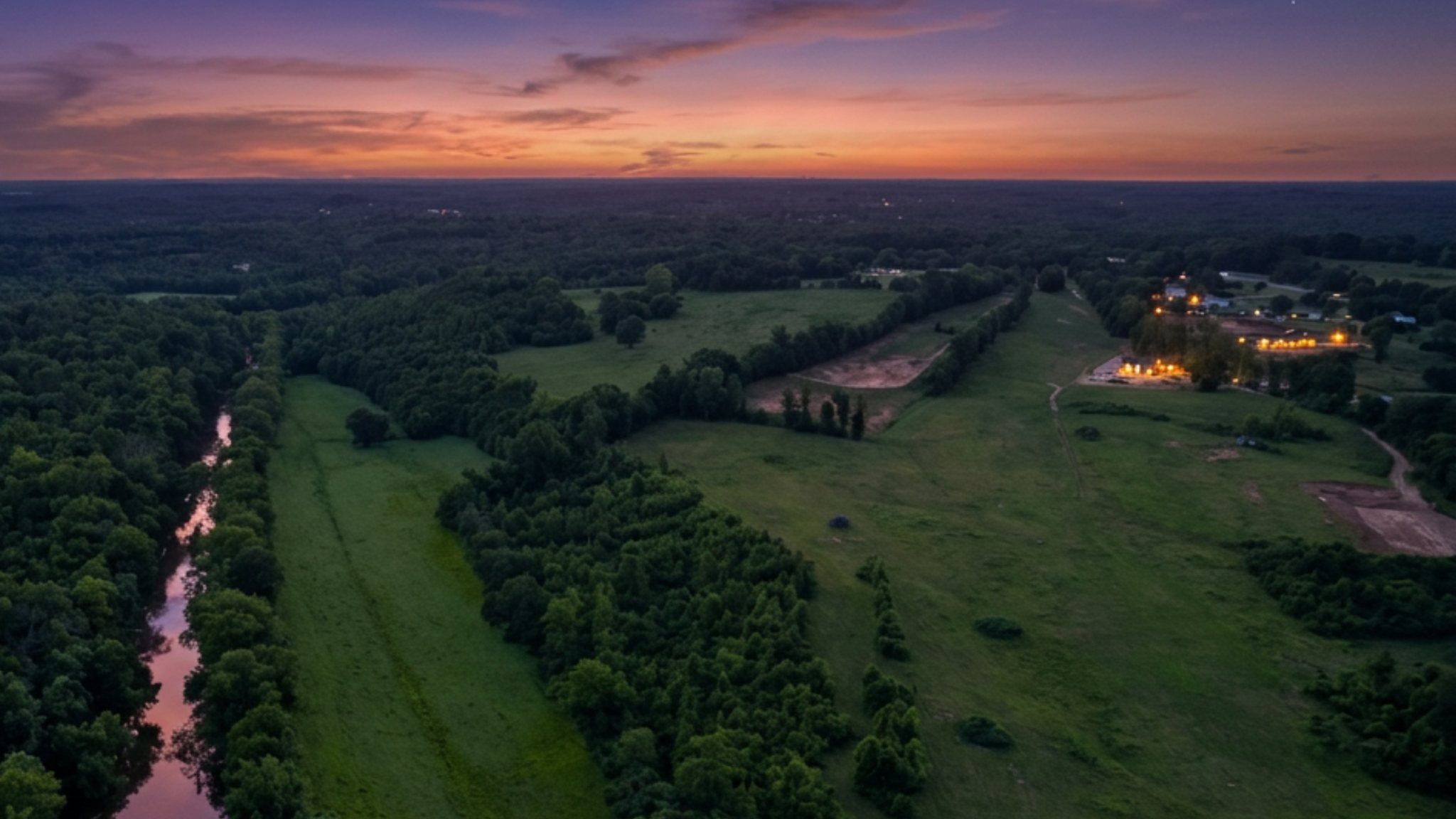 Twilight aerial across open pasture and creek corridor