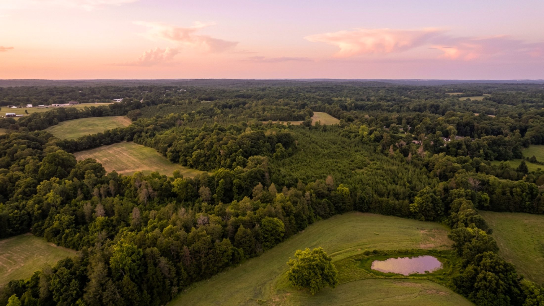 Aerial at dusk over the Biggers Road assemblage — fields, woodland and pond