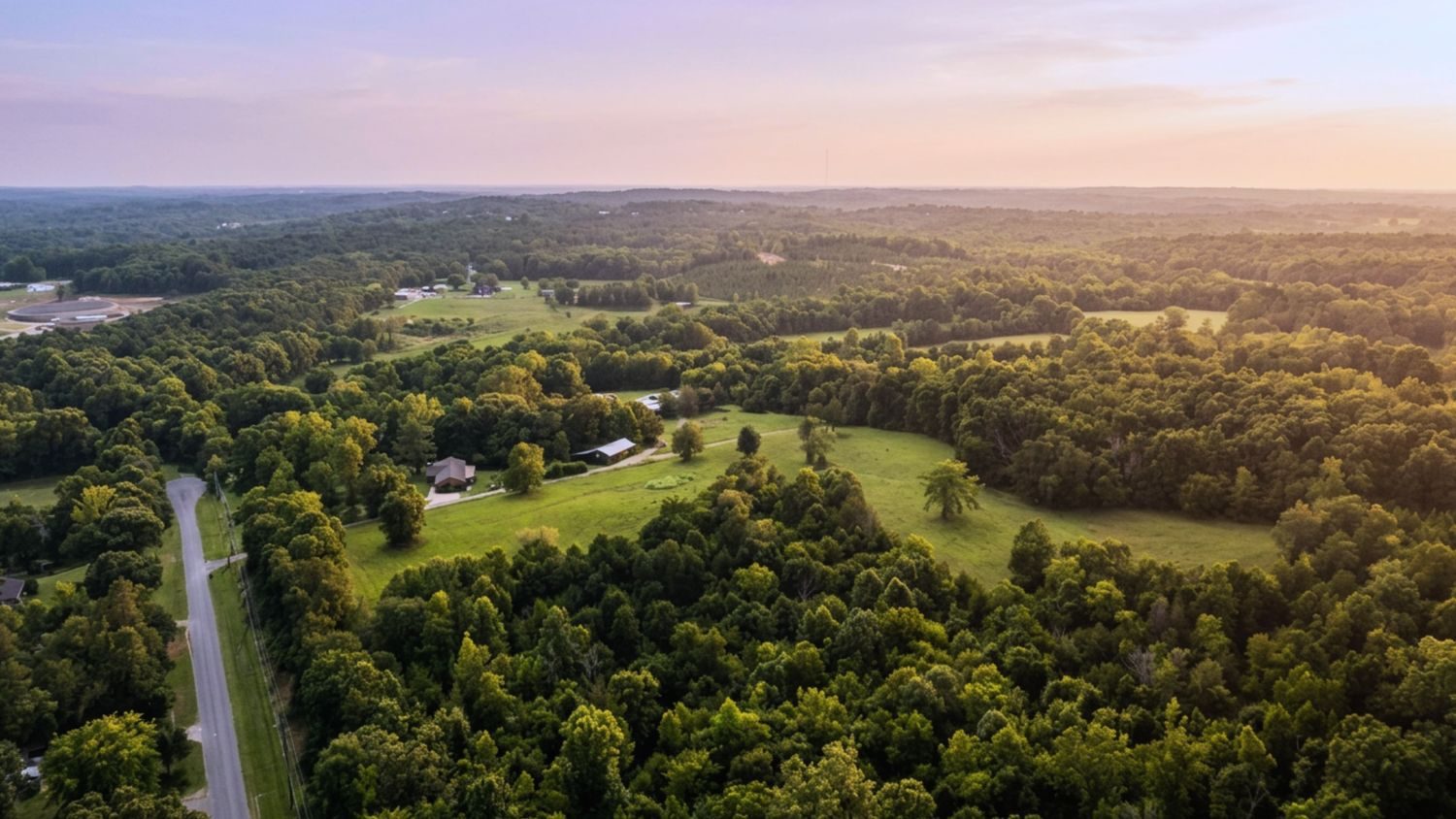 Aerial over wooded ridgeline and pasture at golden hour