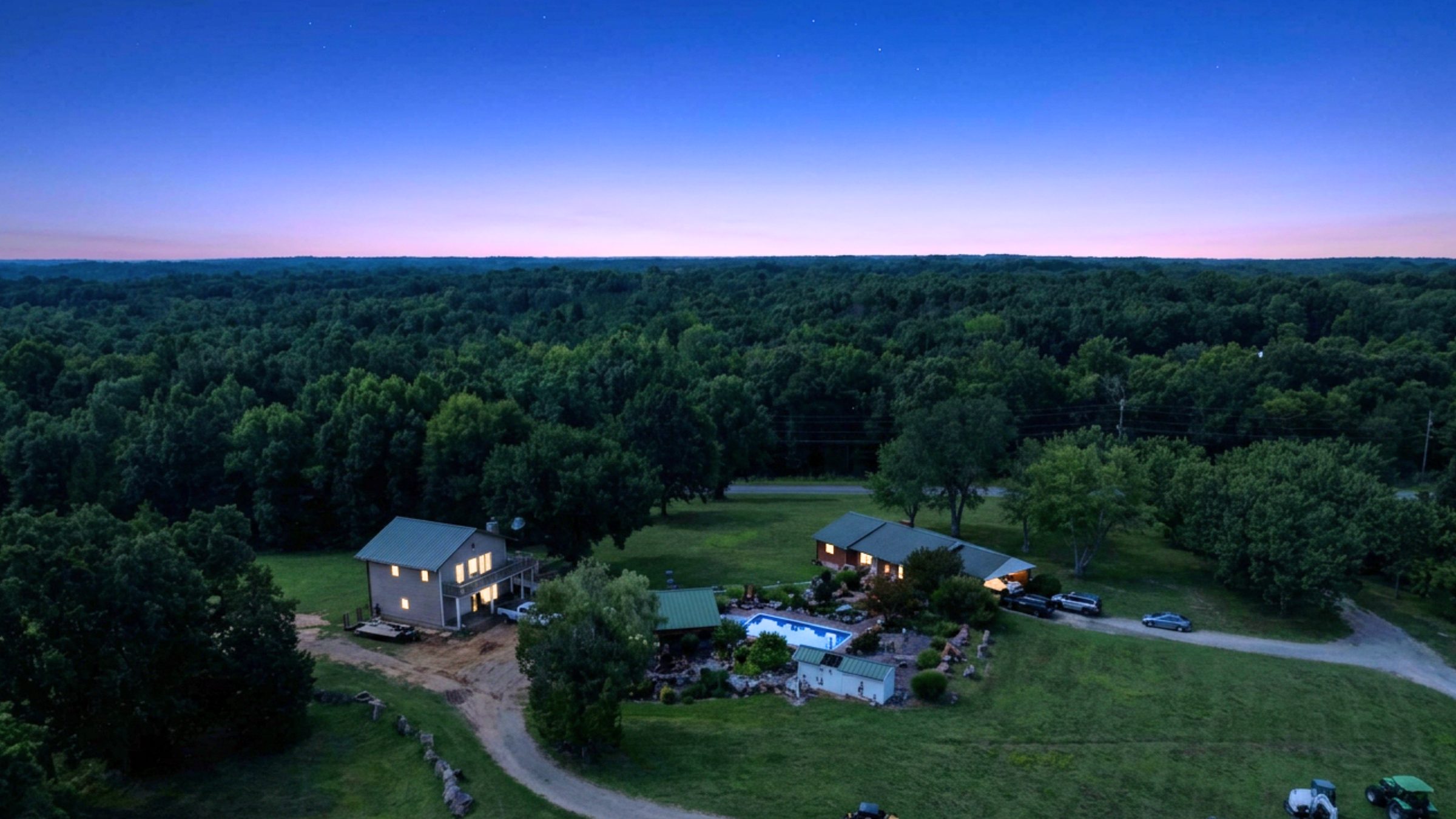 Twilight aerial over the Biggers Road homestead — lit house, pool and pasture at dusk