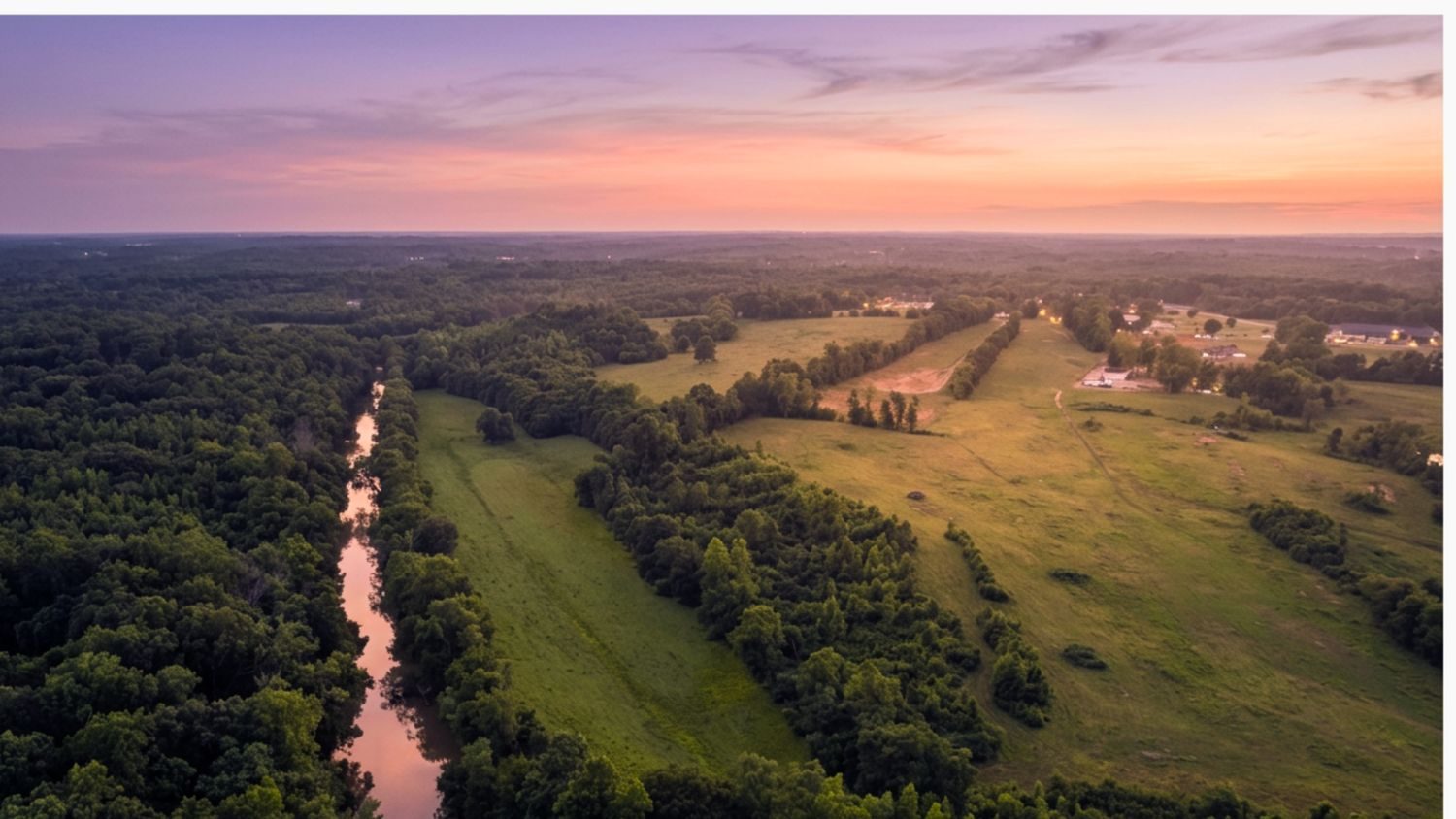 Creek winding through pasture and treelines at dusk