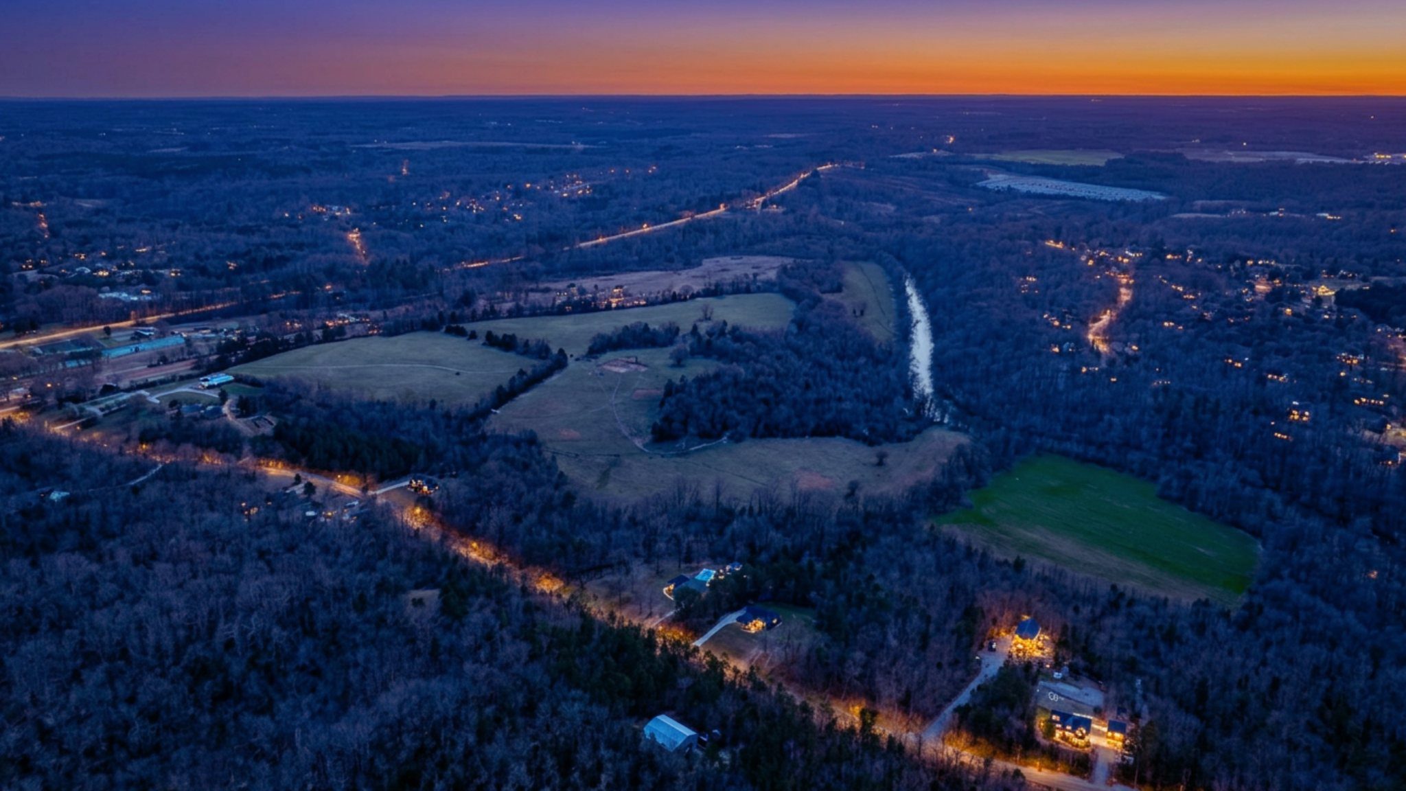 Wide blue-hour aerial showing creek corridor and nearby neighborhoods